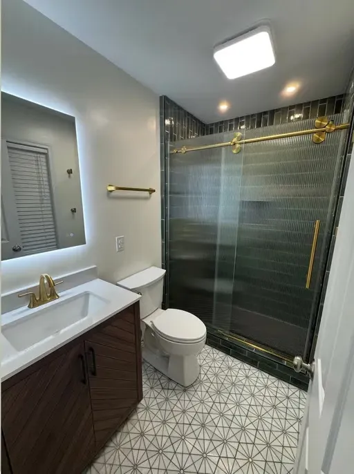 ACG bathroom after renovation: glass shower enclosure, dark vanity, lighted mirror, and patterned tile floor